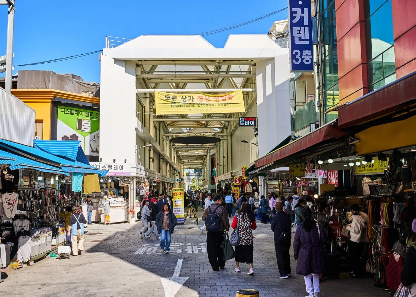 남대문 시장의 풍경, 길 양옆으로는 시장 상점들이 있고, 상점 앞에는 옷이 입혀진 마네킹들이 줄 지어 있다.